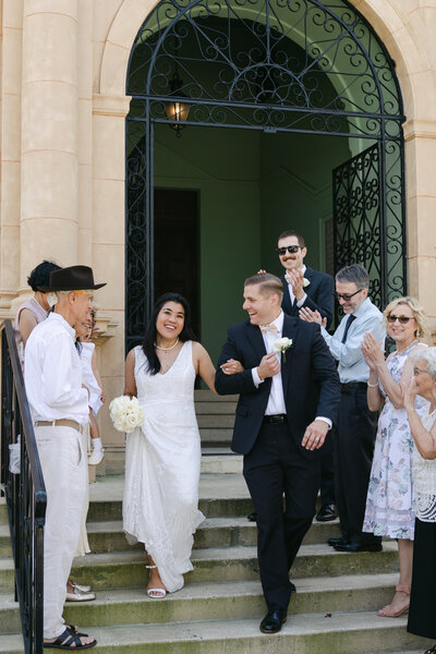 Sarasota courthouse photography of an interracial bride and groom exiting as their family cheers them on from the stairs of the  historic Sarasota courthouse.