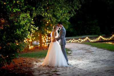 couple embraces in front of twinkle lights at night at Hidden Acres wedding venue in Marion, SC