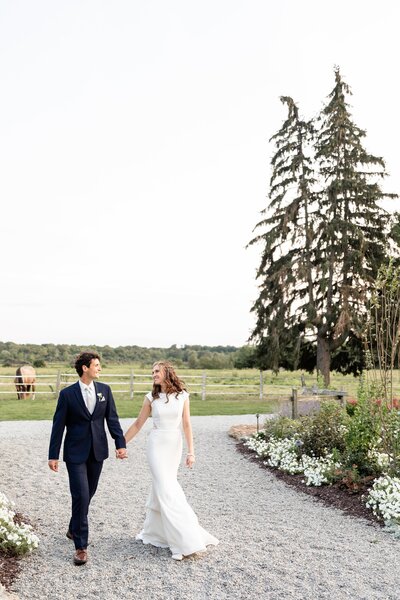 Newlyweds-walk-along-stone-pathway-during-sunset-at-a-maple-meadows-wedding
