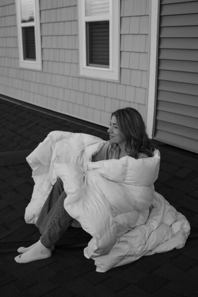 Minnesota wedding photographer cuddles into white duvet as she sits on the rooftop of her home