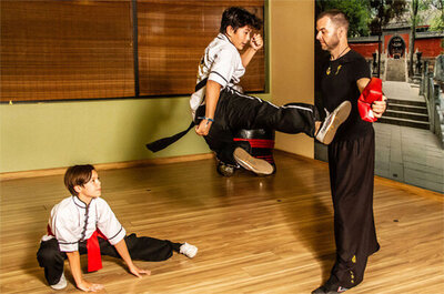 Action photo student kicking while in mid air second student on floor looking up watching him instructor Jason Campbell standing in front holding up arm to kicking students foot