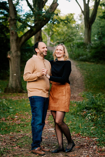 Middle-aged man and woman smiling and clasping hands mid-dance in the middle of an oak grove.