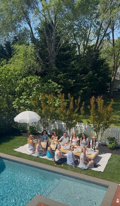 Backyard luxury picnic with styled table, white umbrella, and a group of guests celebrating together, designed by Yours Truly, a wedding planner and designer in New Jersey.
