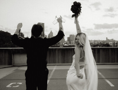 Bride and groom throwing their hands up with Pittsburgh skyline in the background 