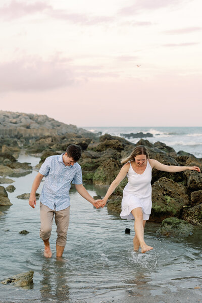 Engaged couple holding hands while walking barefoot in shallow water, Wilmington beach engagement session