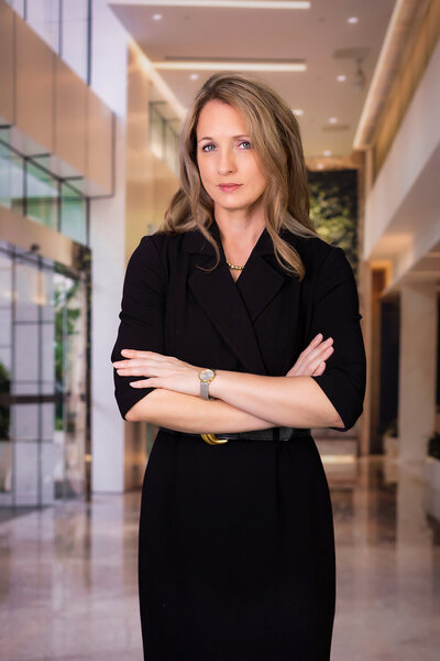 Professional branding photo of a Maine businesswoman in a dark suit, posed in front of a modern office background.