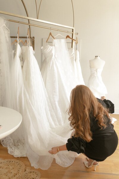 Stylist helping a bride adjust bride's wedding dress in a bridal boutique.
