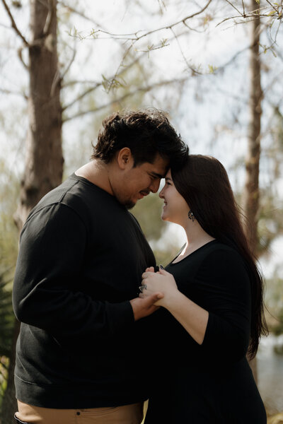 Engaged couple holding hands and smiling while standing together in a tranquil outdoor environment.