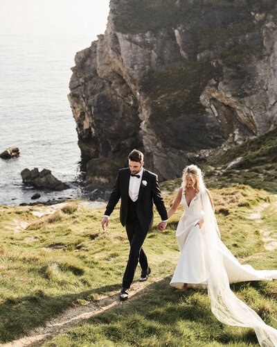 bride and groom walking along cliff