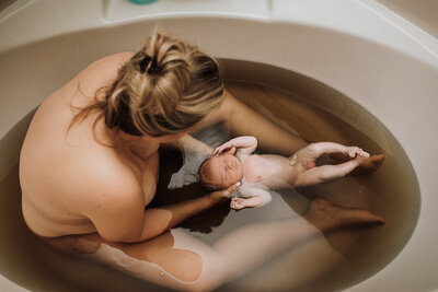 mom and newborn in herbal bath water