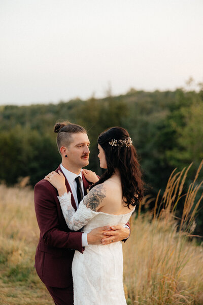 A groom in a red suit looking at his bride.