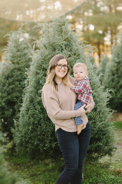 a-mom-holding-her-son-and-smiling-at-the-camera-for-christmas-tree-mini-portraits-with-nashville-family-photographer-dolly-delong