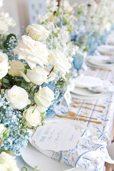 Luxurious floral wedding tablescape with white roses and dusty blue accents.