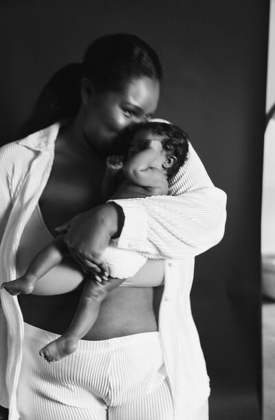 black and white photo of mom kissing newborn baby on head