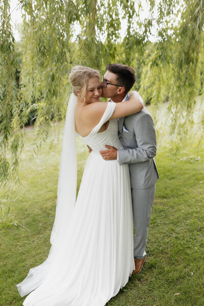 Joyful couple embracing under willow trees during intimate outdoor wedding, natural and romantic moment for couples planning a small wedding or elopement
