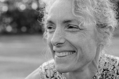 Black and white photo of woman with curly white hair gazing off camera and smiling.