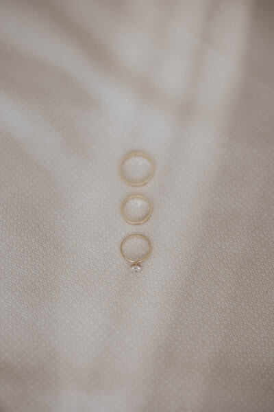 A close-up of three wedding bands and an engagement ring on a textured fabric.