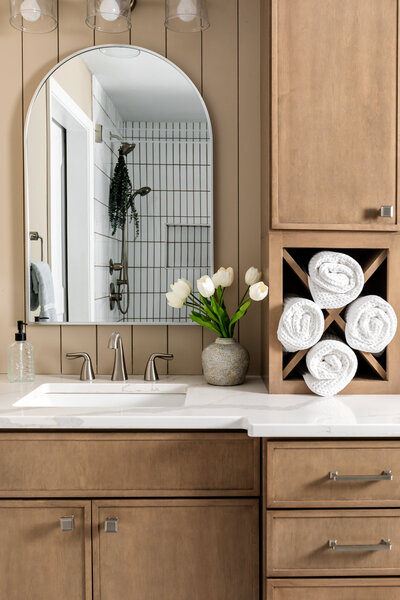 Primary bathroom stained neutral brown vanity cabinet with tower storage, mirror and decor.
