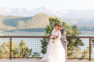 Groom hugs bride from behind and kisses her shoulder on the overlook at their Ridgway State Park Wedding 