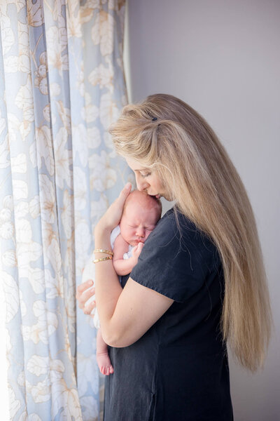 sentimental newborn photography  of mother lovingly kissing newborn son by a window