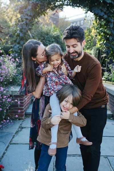 nyc family portrait in central park conservatory garden with flowers and kids hugging and laughing