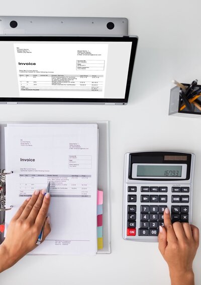 Image of reports that a bookkepper uses with a calculator and a computer screen shoing and invoice