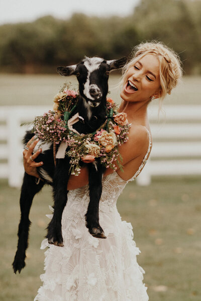 Sabina in her Galia Lahave wedding dress holding a goat with a flower collar.