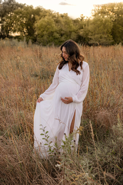 Mom plays with her white dress during maternity photos in the field at mequon nature preserve