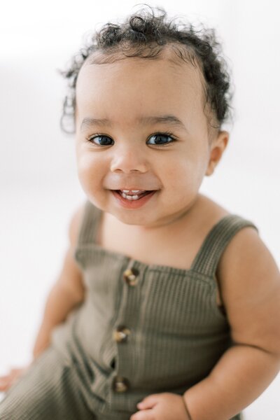 Precious African American baby smiling at the camera in a green romper in studio for his first birthday session