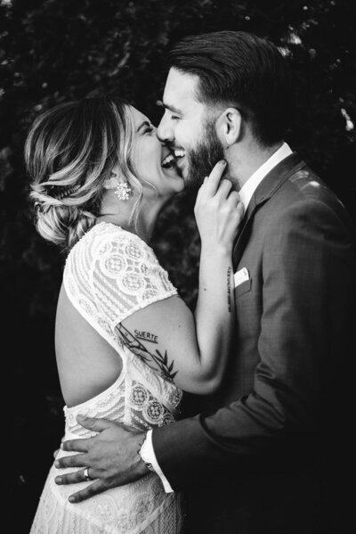 bride in white lace gown laughs at groom in tux while holding his face in black and white at durham hill farm shot by wedding photographer in philadelphia alex medvick