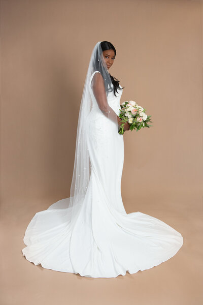 Bride wearing chapel length veil with lots of pearls and holding a white and blush bouquet