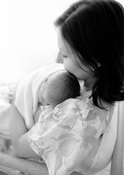 new mom wearing floral dress holds newborn baby during boston, MA newborn photo session