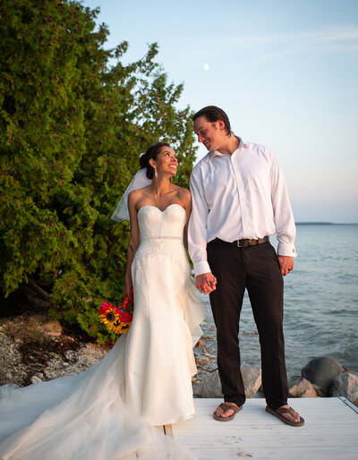 bride and groom hold hands in front of lake and trees
