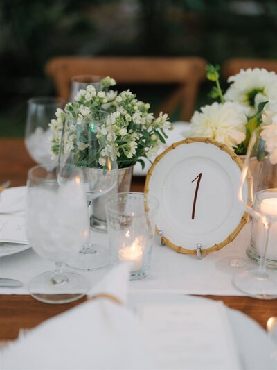 Hand lettered brown table number on white plate with bamboo rim for a wedding at Lion Rock Farm in Litchfield County, Connecticut.