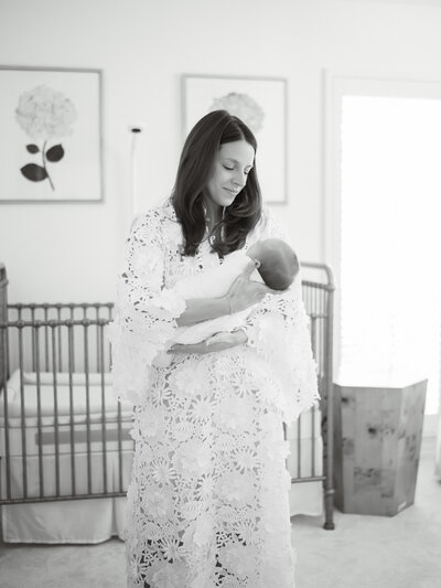 Newborn lays in crib while parents look on her, newborn photographer