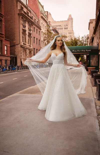 Bride in a sparkly A-line wedding gown holding her veil on a city street