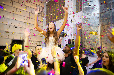 a bat mitzvah girl gets lifted above the crowd under a shower of confetti