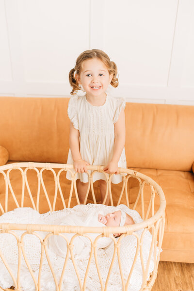 Young girl sitting on a white chair smiling at the camera in white dress