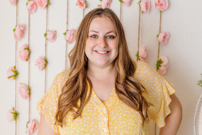 Newborn Photographer, Cassie smiles before a floral covered wall