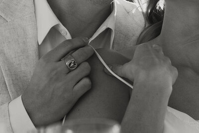 Black and white close-up of groom holding bride’s shoulder strap while she gently touches his shirt during their Joshua Tree elopement.
