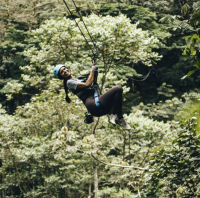 Woman smiles as she ziplines from out of and through the Costa Rican jungle, trees, and greenery