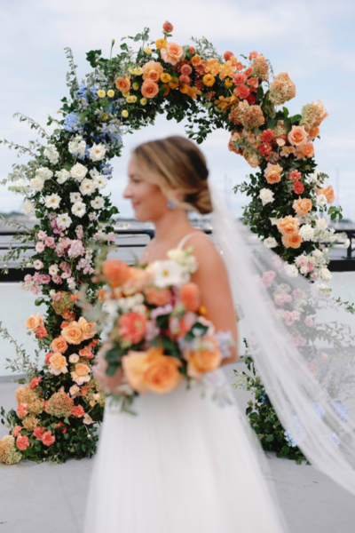 Bride carrying bright yellow and orange bouquet, blurred, walking in front of camera