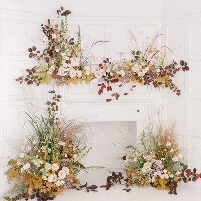 Large wedding arrangements with roses and autumn greenery, around a fireplace moulding at Livart. 