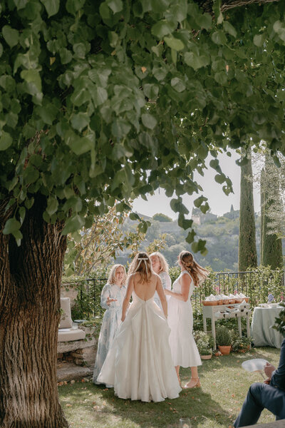 Bride and her bridesmaids walking through the village of Gordes, France in mismatched white lace dresses for a summer wedding