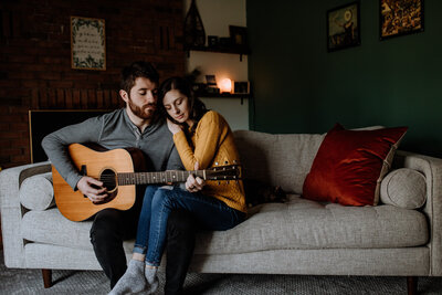 man holding guitar and sitting next to woman on couch