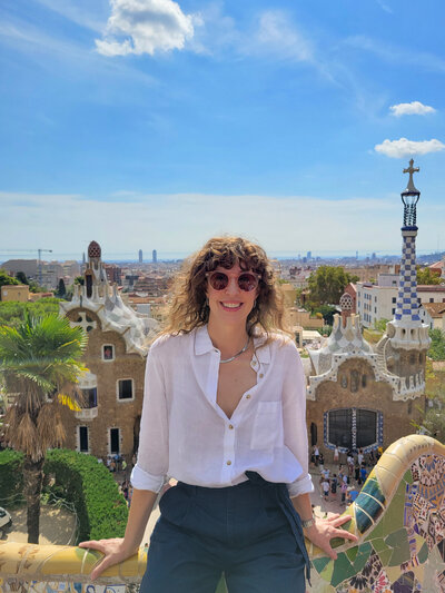 Award-winning luxury travel expert Stephanie Dosch seated on the tiled railing of Park Guell, designed by architect Antoni Gaudi, overlooking Barcelona, Spain ©Stephanie Dosch | theViatrix Cultural Travel