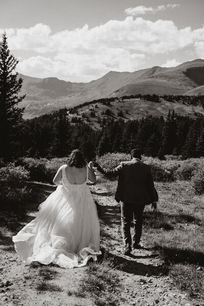 Bride and groom walk hand in hand on rugged trail after mountain elopement near in Hoosier Pass.