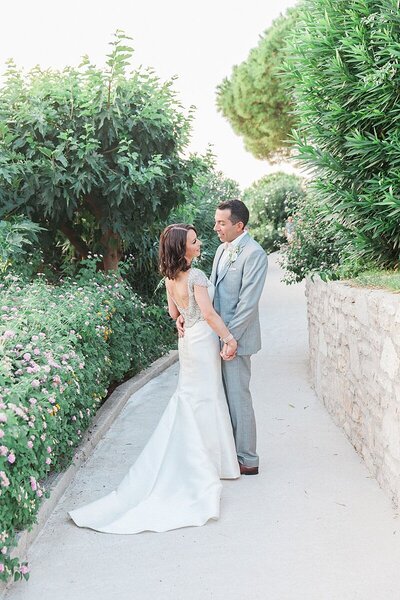 Bride and groom share a quiet moment beside their waterfront reception setup with string lights and parasols, overlooking the sea at their destination wedding in Greece