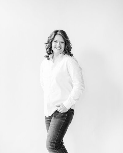 black and white photo of Amy Harper smiling directly at the camera with her hand half in her jeans pocket