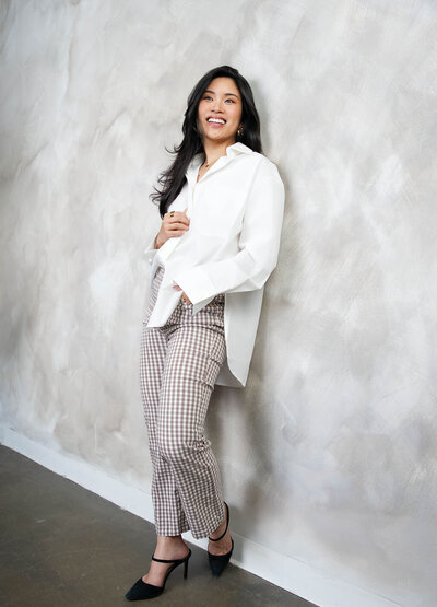 Stephy Chen standing confidently in a white blazer and patterned pants, smiling during a modern personal brand photoshoot against a textured wall.